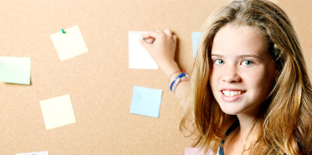 Young female student posting a note on a cork board.