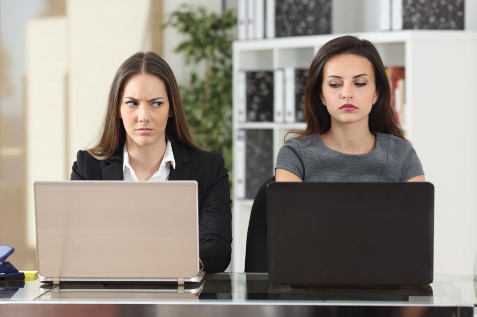 Two women working side-by-side glancing sideways at each other