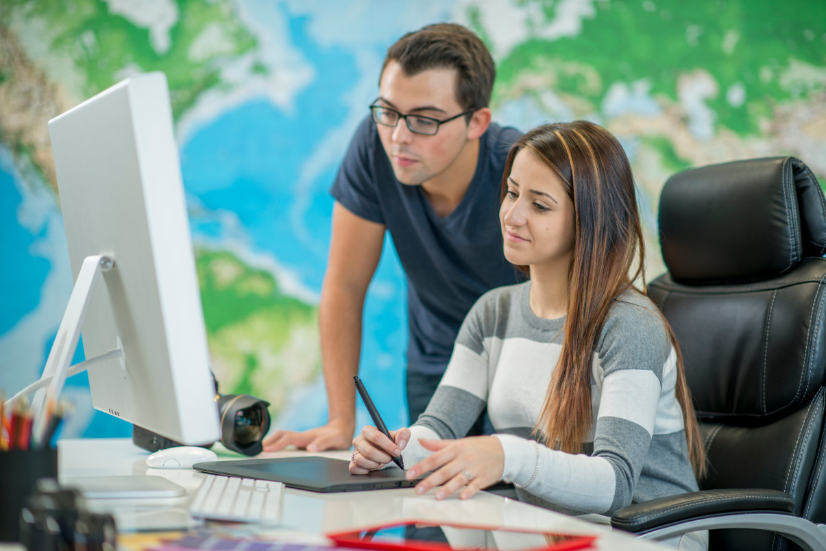 Colleagues working on computer while woman sits in leather desk chair.