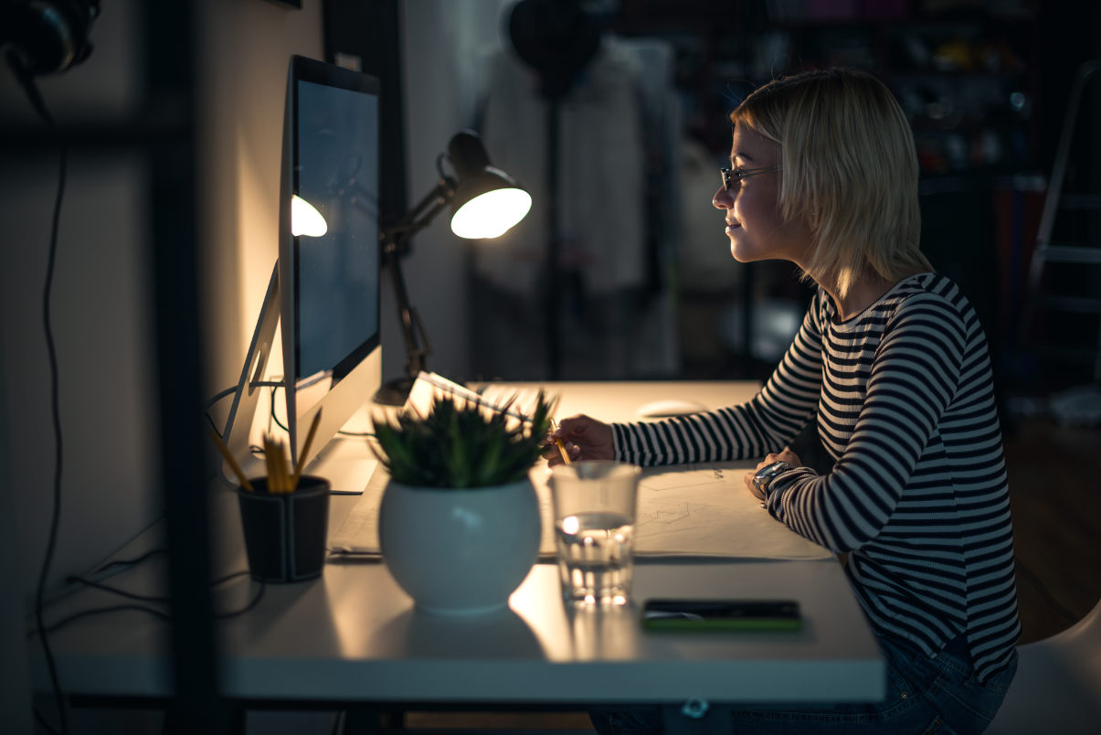 Woman working at her desk at night using a desk lamp. 