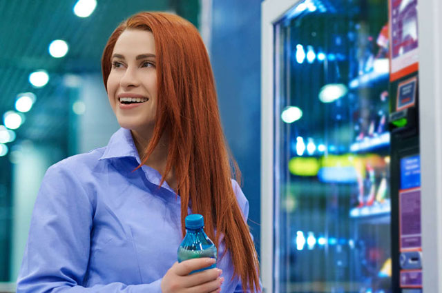 Smiling woman buying bottled water from vending machine.